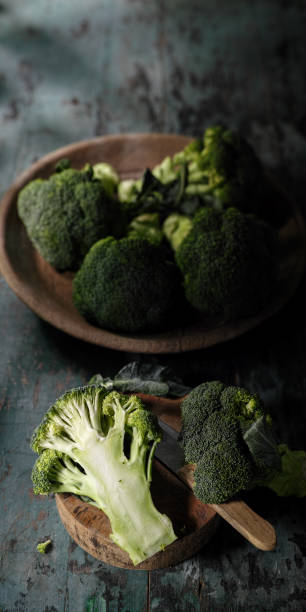 istock Market fresh broccoli sliced in half on an old wooden cutting board alongside a sharp knife on a turquoise coloured wooden table background, with more broccoli spears in a wooden bowl next to the cutting board. 691703868
