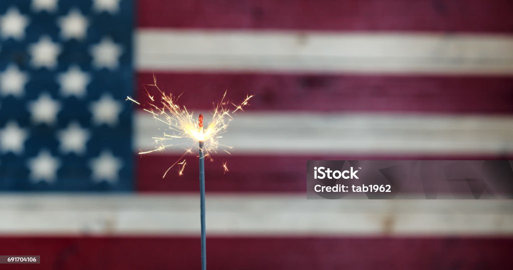 Glowing sparkler with rustic wooden flag of United States of America Burning sparkler with rustic wooden United States Flag in background Fourth of July Stock Photo