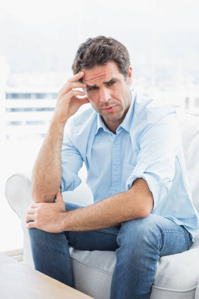 istock Man with headache sitting on the couch looking at camera 691713246