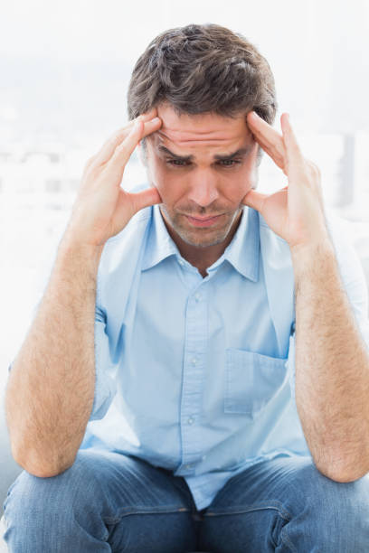 istock Wincing man with headache sitting on the couch 691713268