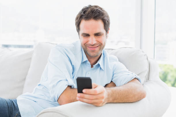 istock Happy man sitting on the couch sending a text 691715418
