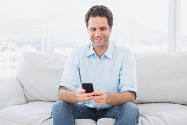 istock Happy man sitting on the couch sending a text message 691715580