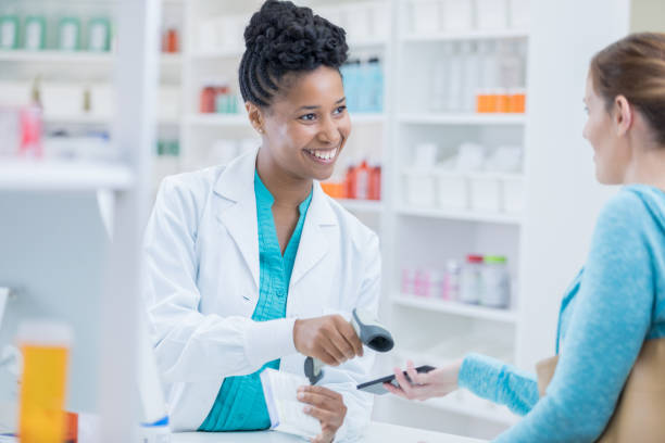 african american pharmacist scans woman's smart phone at checkout - prescription doctor rx pharmacist imagens e fotografias de stock