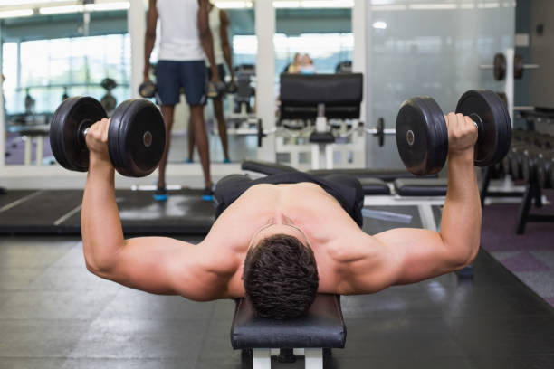 istock Shirtless bodybuilder lying on bench lifting heavy dumbbells 691716670