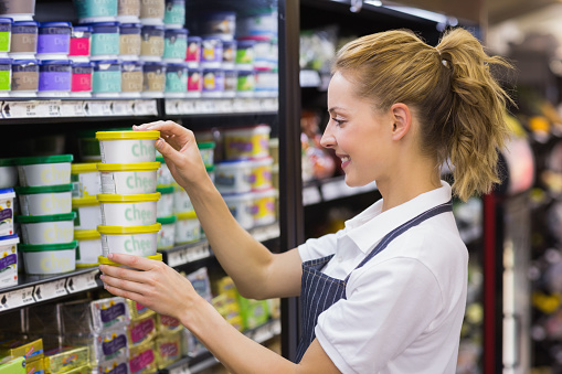 Smiling blonde worker taking a products in shelf in supermarket