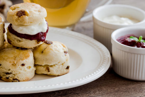 le focaccine di uvetta fatte in casa servono con marmellata di fragole fatta in casa, panna coagulata e tè. set di focaccine color crema su piatto bianco. scones è una pasticceria inglese per tè pomeridiano, tè alla crema. focaccine del devon shire e f - cornish cream tea foto e immagini stock