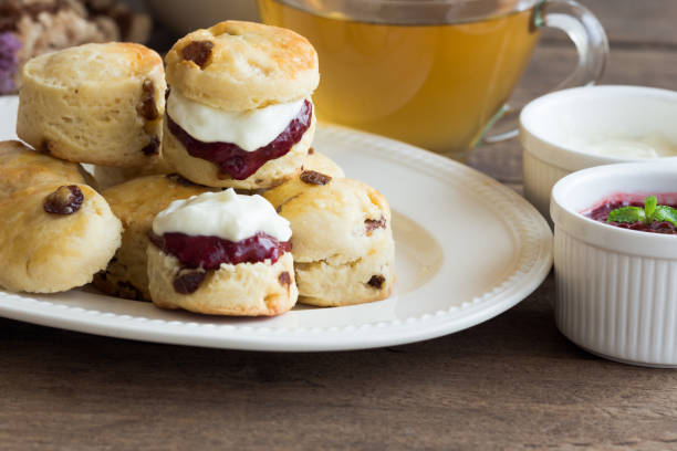 le focaccine di uvetta fatte in casa servono con marmellata di fragole fatta in casa, panna coagulata e tè. set di focaccine color crema su piatto bianco. scones è una pasticceria inglese per tè pomeridiano, tè alla crema. focaccine del devon shire e f - cornish cream tea foto e immagini stock