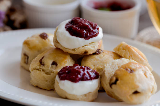 le focaccine di uvetta fatte in casa servono con marmellata di fragole fatta in casa, panna coagulata e tè. set di focaccine color crema su piatto bianco. scones è una pasticceria inglese per tè pomeridiano, tè alla crema. focaccine del devon shire e f - cornish cream tea foto e immagini stock