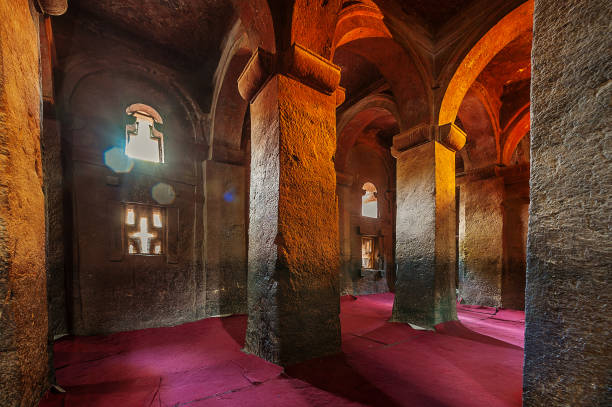 Inside Rock-Hewn Church Oragne Yellow lit stone pillars and windows inside a rock church with purple red carpets Lalibela Ethiopia Horn of Africa ancient ethiopia stock pictures, royalty-free photos & images