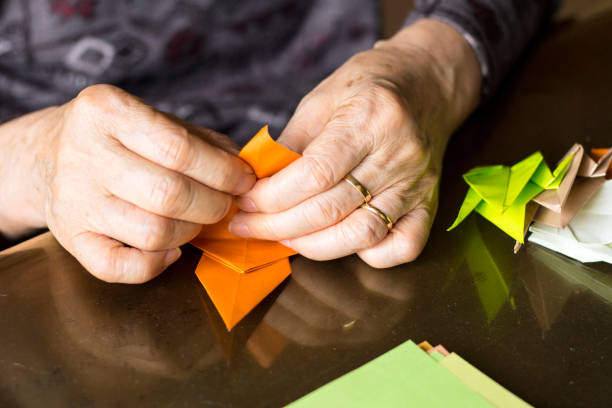 manos de dama senior plegado de papel origami - paper craft brown wrinkled fotografías e imágenes de stock