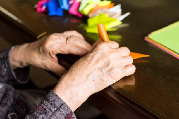 manos de dama senior plegado de papel origami - paper craft brown wrinkled fotografías e imágenes de stock