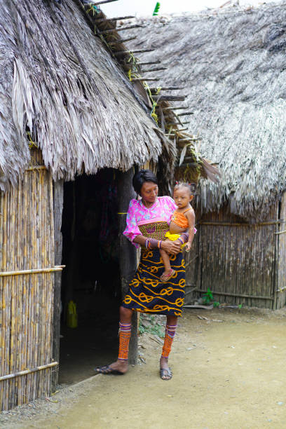 Mother and child in Kuna Yala village , San Blas archipelago in Panama. San Blas, Panama - February 16, 2017: Mother holding a child in front of her house as part of Village in San Blass archipelago. Houses are from wood and bamboo and close to each other. San Blas is an old name for Panamas northeast province known for Kuna Yala indigenous people living there. Official they are Gunas and they live in Guna Yala province. The people are very small and mostly they don’t have connections with other people and culture. kuna yala stock pictures, royalty-free photos & images