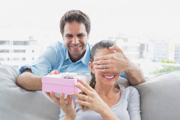 istock Man surprising his girlfriend with a pink gift on the sofa 691761660