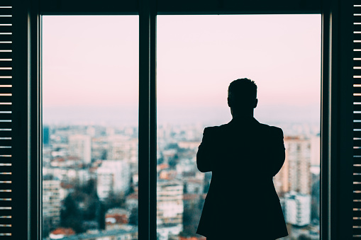 Sillouette of a businessman looking at the view outside his office.