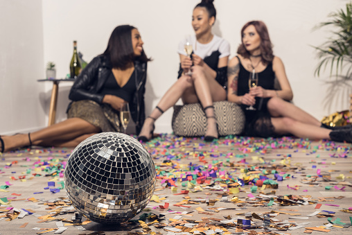young girls sitting and drinking champagne at party with disco ball on foreground