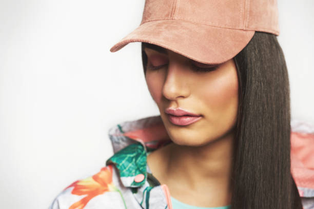 Demure, young Indian woman with downcast eyes wearing a trendy peak cap with her long hair to one side, three quarter face pose