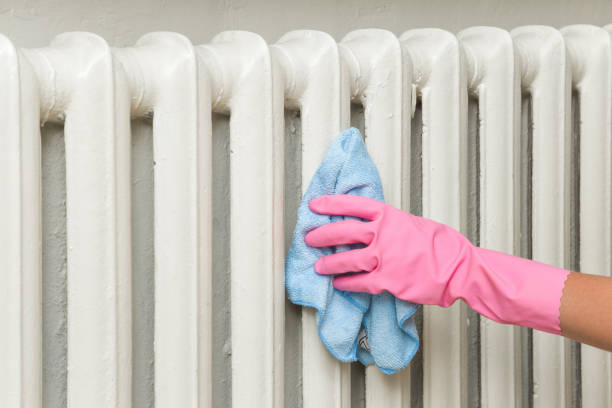 Hand in pink rubber protective glove with rag wiping a heater radiator. Early spring cleaning or regular clean up. Maid cleans house. stock photo