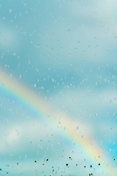 Water drops on a window with the rainbow on the blue sky in the background