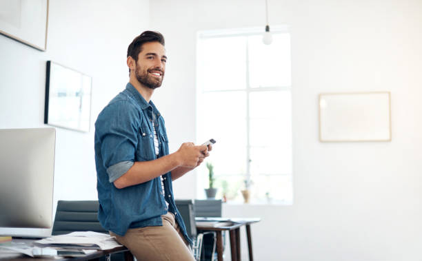 Using the smartest tech to match his startup needs Cropped shot of a young designer texting on a cellphone in an office man thinking stock pictures, royalty-free photos & images