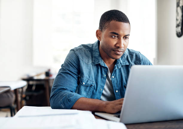 Working hard to differentiate his business from competitors Cropped shot of a young designer working on a laptop in an office black man laptop stock pictures, royalty-free photos & images