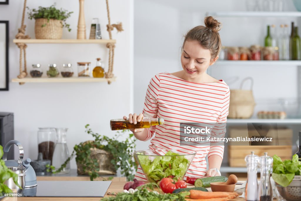 Woman adding olive to a salad Young woman standing in a kitchen and adding olive to vegetable salad Cooking Stock Photo