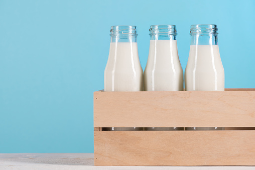 glass bottles with milk in wooden box on tabletop at blue background