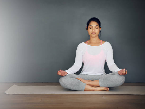 Finding her zen Shot of an attractive young woman doing yoga and meditation at home yoga pants stock pictures, royalty-free photos & images