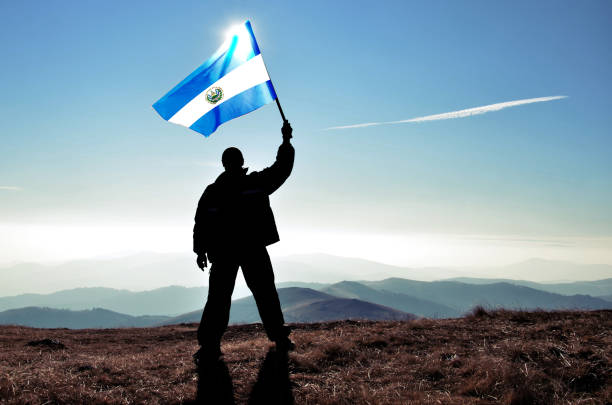 успешный силуэт человека-победителя, размахивающего сальвадорским флагом на вершине горной вершины - salvadoran flag стоковые фото и изображения