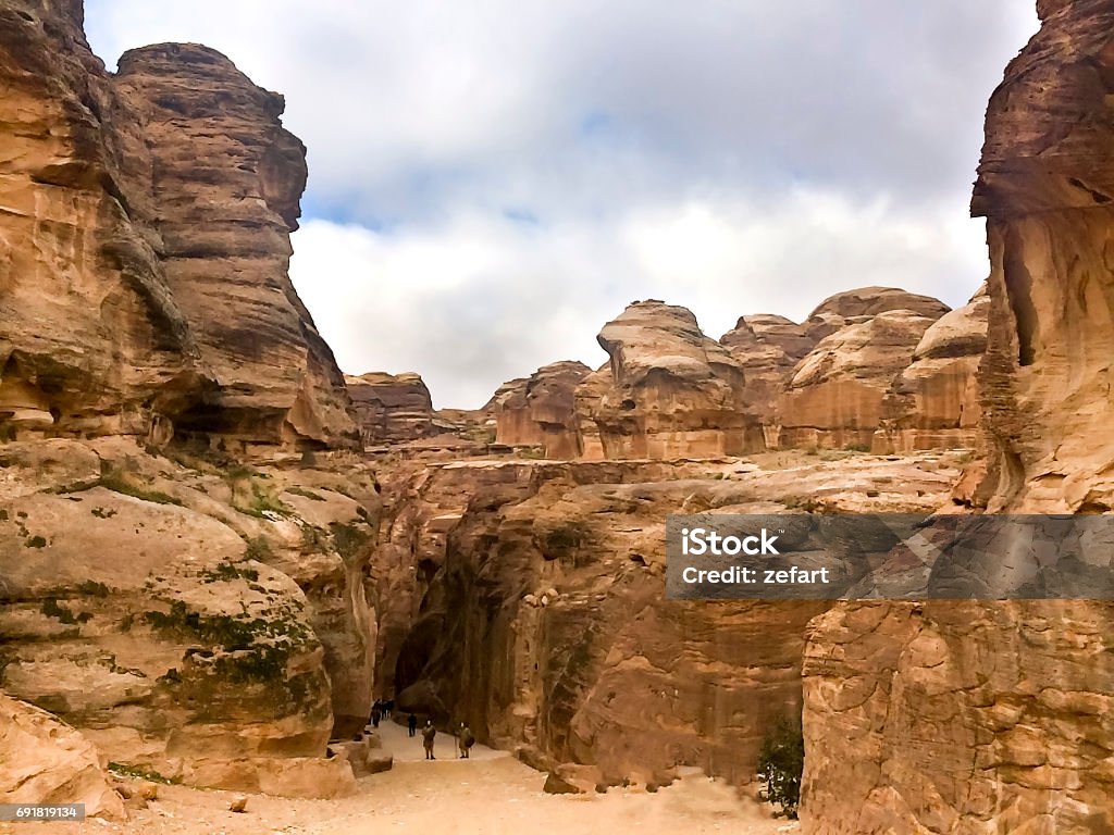 The Siq, the narrow slot-canyon that serves as the entrance passage to the hidden city of Petra, Jordan, seen here with tourists walking.This is an UNESCO World Heritage Site Ancient Stock Photo
