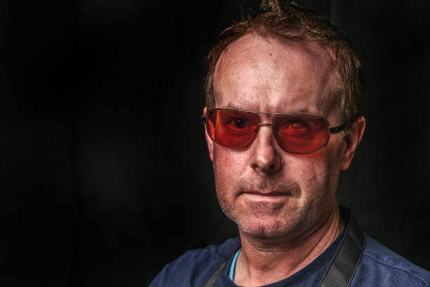 head to shoulders portrait, seen from the side, of a young adult, italian, caucasian man, wearing sunglasses while looking outside of the window and illuminated by the sunlight