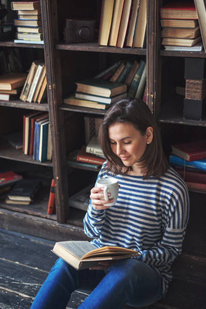 istock Young woman reading a book with a cup of coffee 691829284