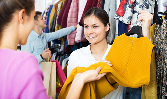 Cheerful female assistant serving customer asking in clothing boutique