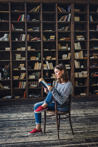 Serious young woman with a book in front of the bookshelves