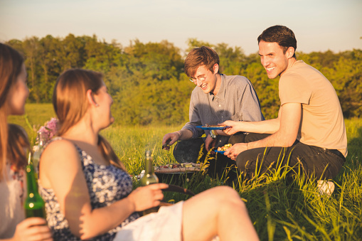 Women looking at male friends preparing food in picnic on grassy field