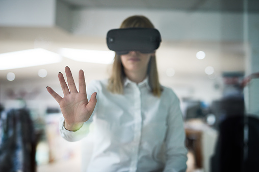 Multiple exposure shot of a young businesswoman wearing a VR headset while working alone in her office