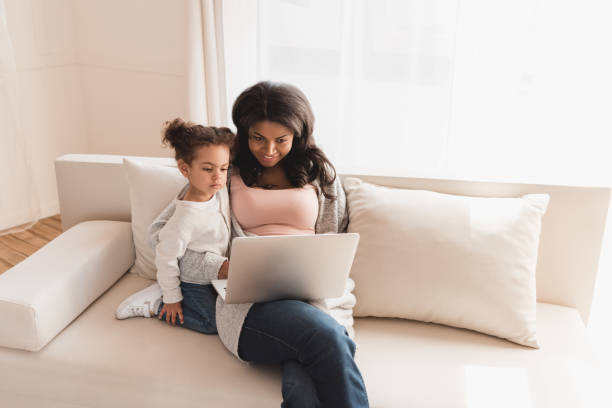 istock Beautiful mother and daughter sitting on couch and using laptop together 691857230