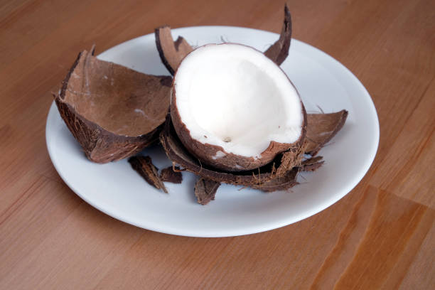 Still life with broken coconut shell ripe white flesh inside and debris on round white plate on brown wooden table horizontal close up photo