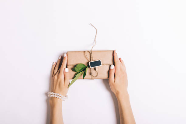 istock Beautiful female hands with manicure holding a box with a gift on a white table 691886544