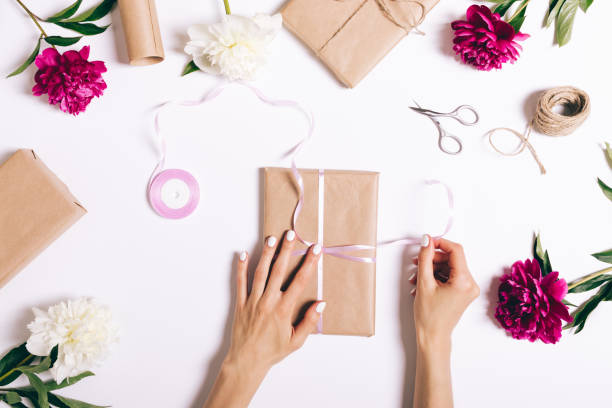 istock Female hands tie a ribbon on a gift for a holiday on a white table 691886562
