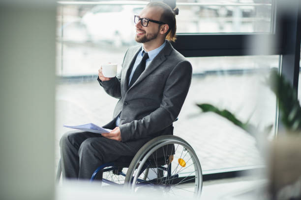 istock smiling businessman sitting in wheelchair holding documents and cofee cup 691892040