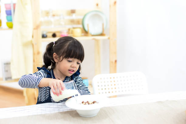 criança saudável menina derrama leite do jarro na cozinha - healthy eating snack child domestic kitchen - fotografias e filmes do acervo