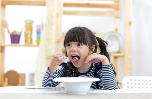 menina bonitinha comer cereais com leite na cozinha - healthy eating snack child domestic kitchen - fotografias e filmes do acervo