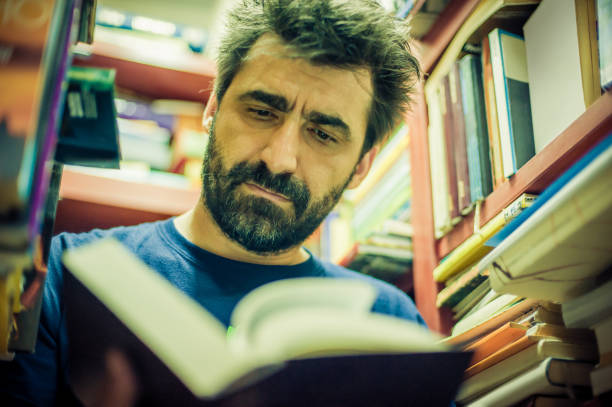 istock Curious man reading book between the shelves in the library 691909740