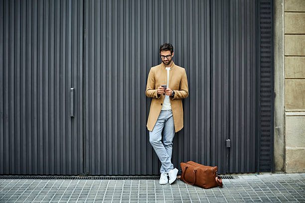 businessman texting on mobile phone against wall - businessman one man only standing elegance 뉴스 사진 이미지