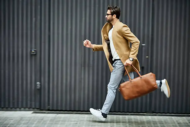 Full length of businessman running on sidewalk. Male professional is carrying bag by building. He is wearing smart casuals in city.