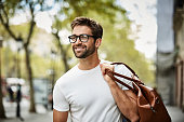 istock Smiling businessman with brown bag walking in city 691910455