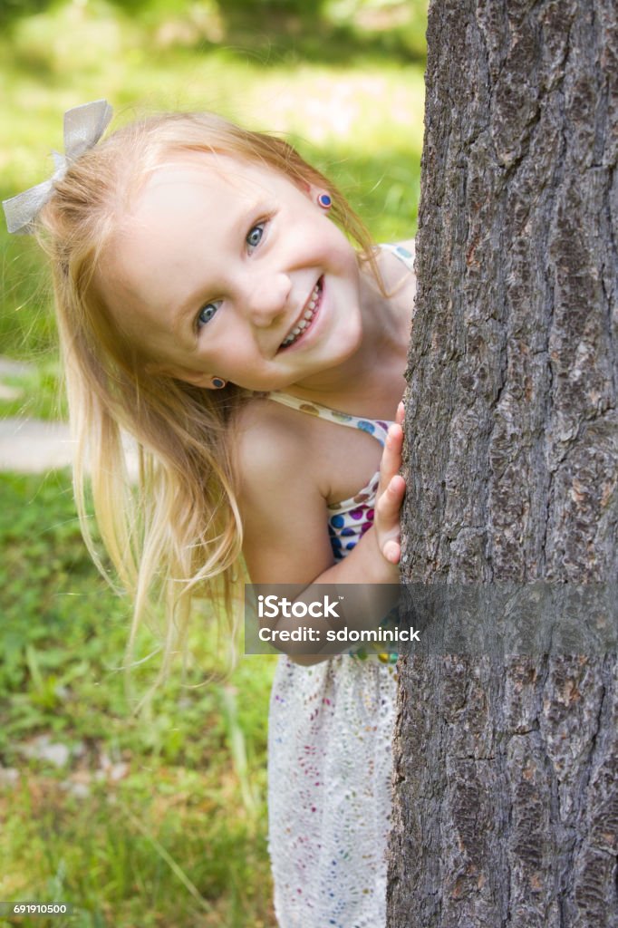 Beautiful Little Girl Playing Peek-A-Boo A beautiful 5 year old girl laughing as she plays peek-a-boo around a tree. 4-5 Years Stock Photo