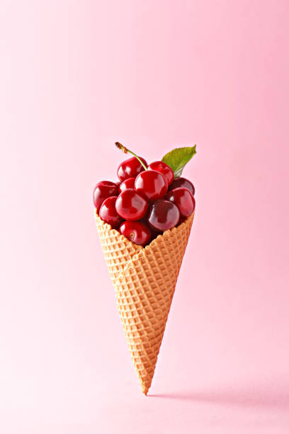 Ice cream cone filled with cherries on a pink background. Fresh cherry in a waffle cone. Summer concept.
