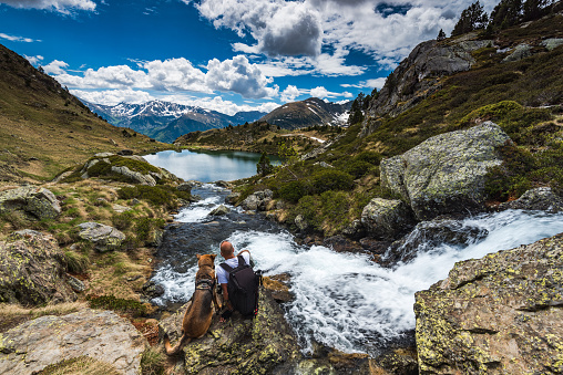 Active man sit on rock with dog while trekking in Pyrenees