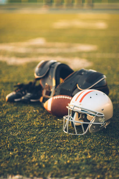 Silver American Football Helmet on Field An American Football helmet sits with a football on a football playing field. The light is from the sun which is about to set, shallow depth of field. Copy space included. Sport background image. american football ball photos stock pictures, royalty-free photos & images